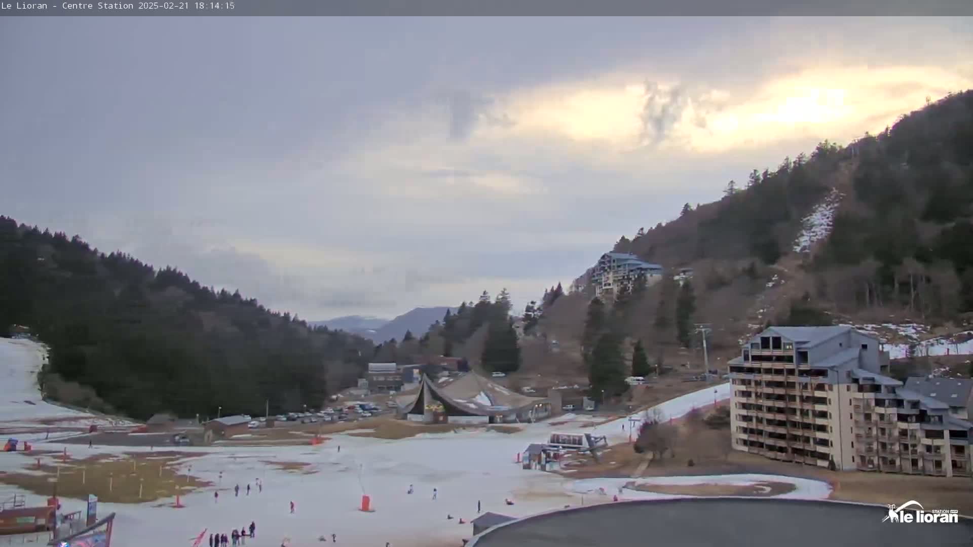 A partly cloudy sunset over a snow-covered ski resort nestled in a mountainous region.