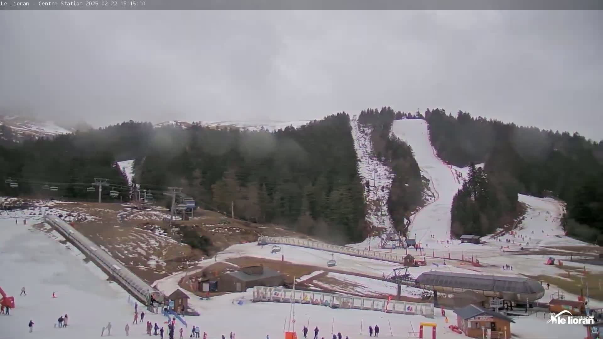 A ski resort on an overcast day shows several ski slopes, chairlifts, and skiers scattered across the snowy terrain.