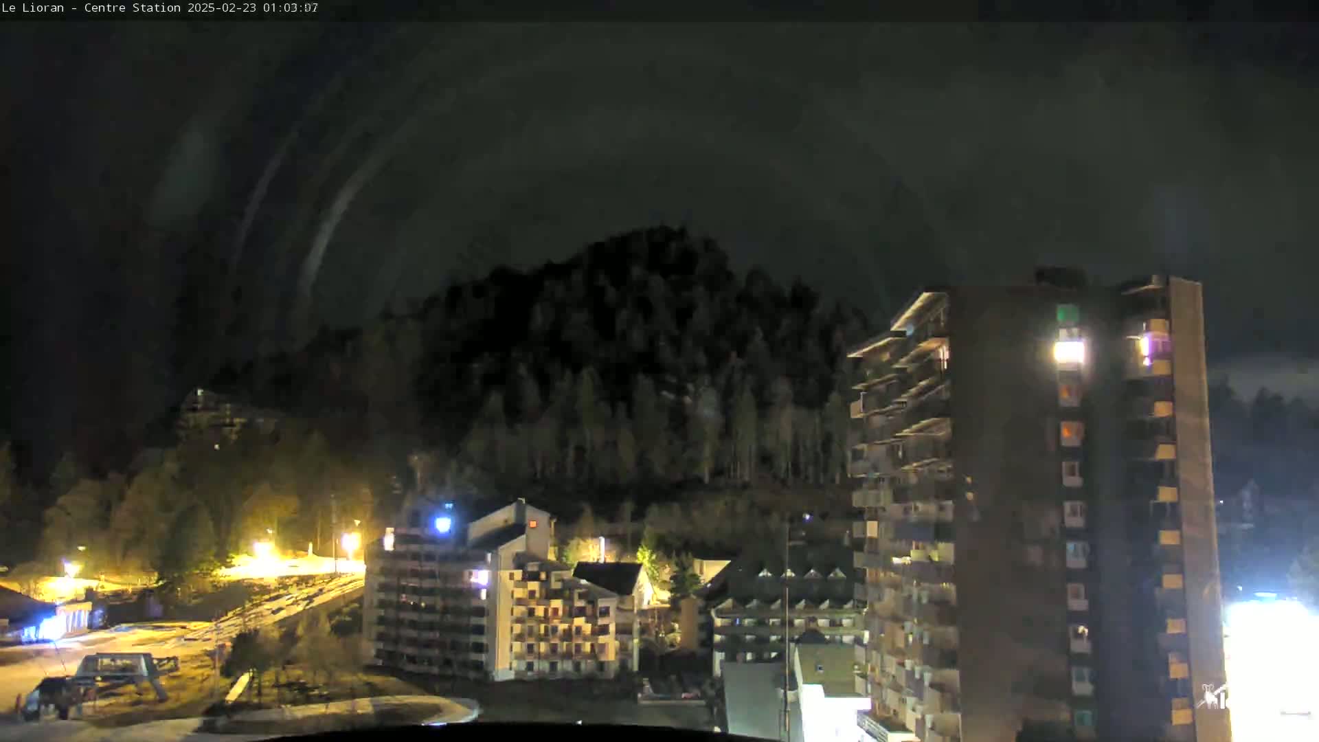 A nighttime view of a snowy, mountainous area with several multi-story buildings illuminated, under a dark, cloudy sky.