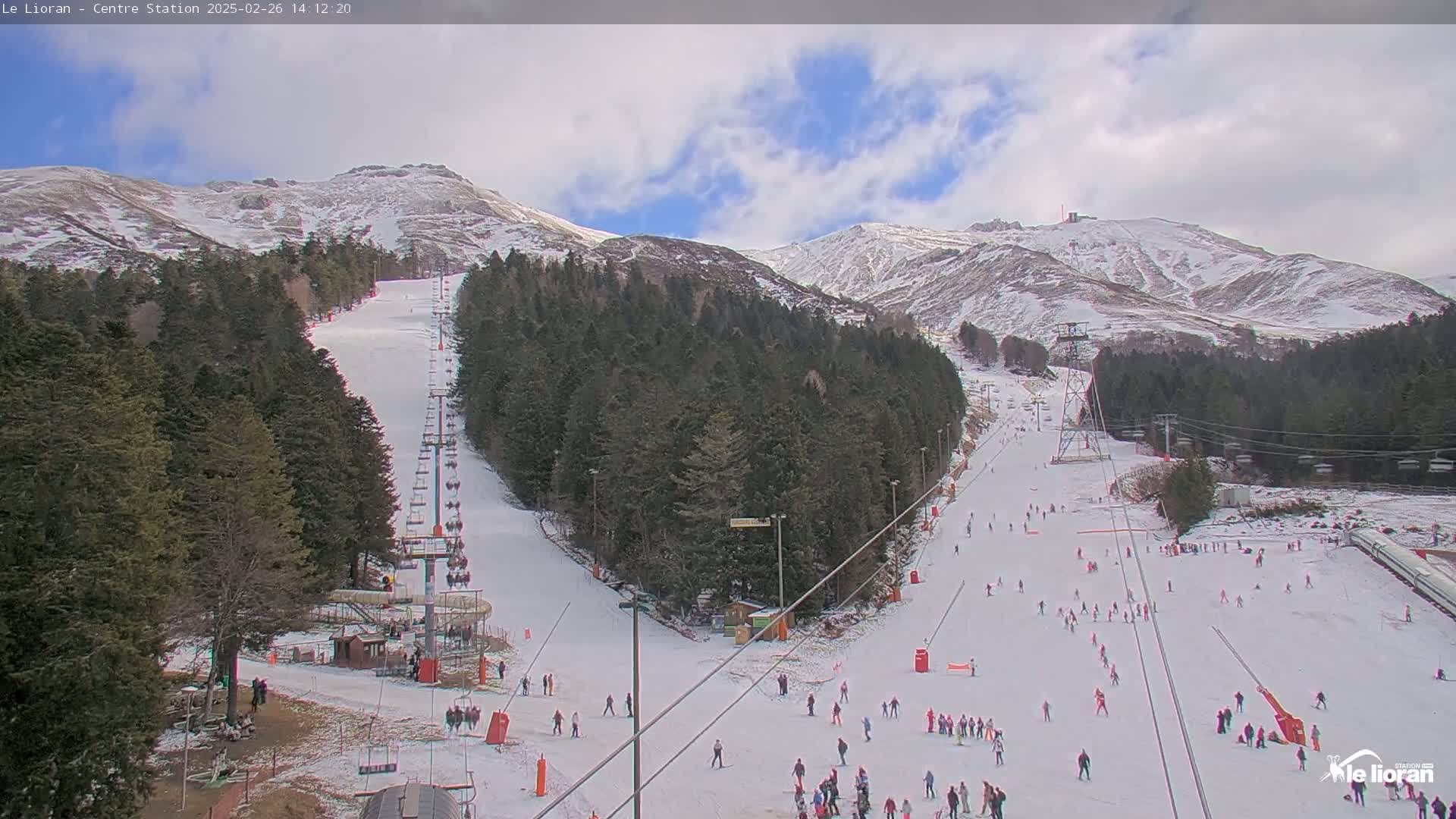 A ski resort with snow-covered slopes and chairlifts, situated in a mountainous area under a partly cloudy sky.