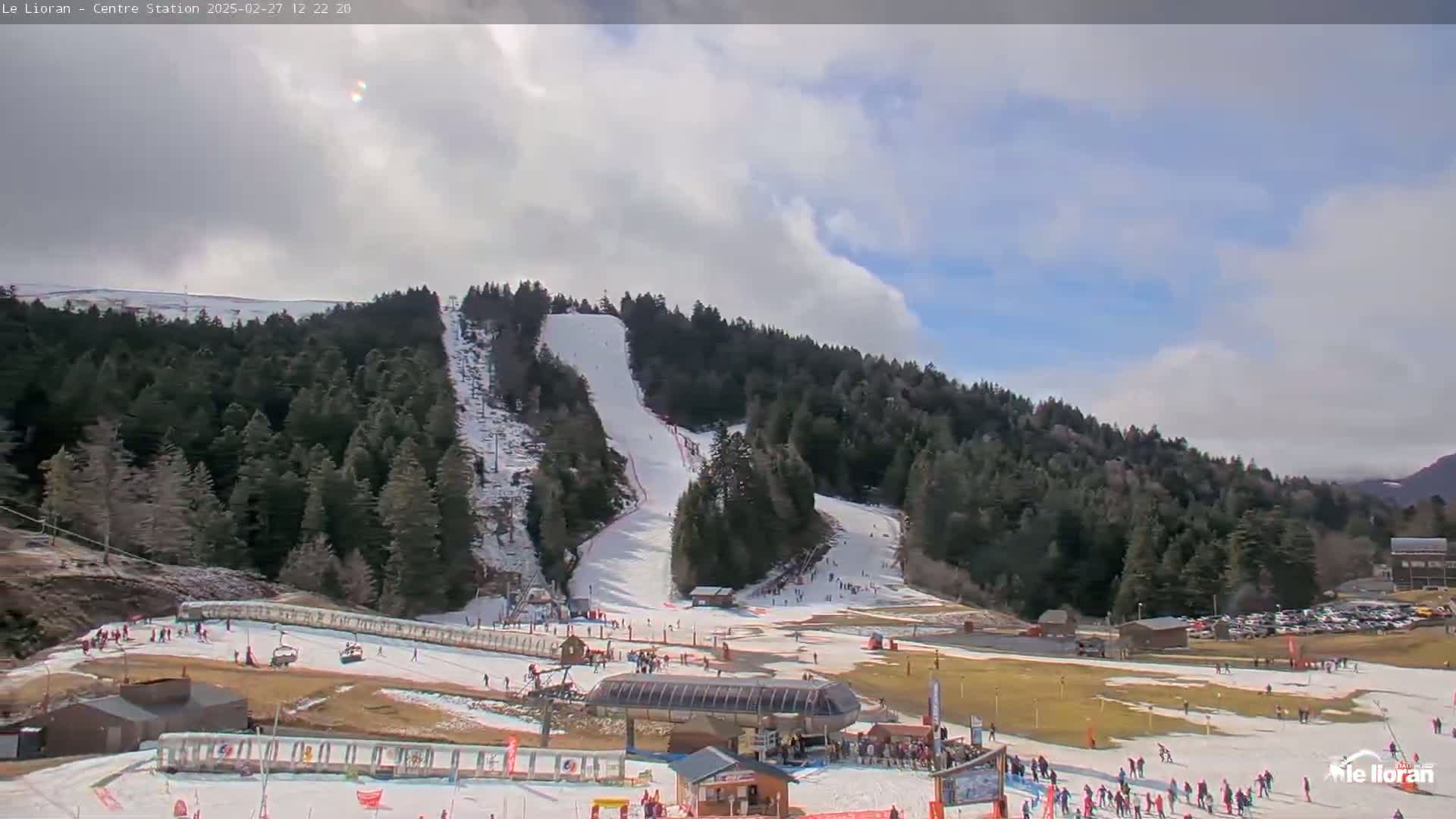 A ski resort with snow-covered slopes and trees under a partly cloudy sky.