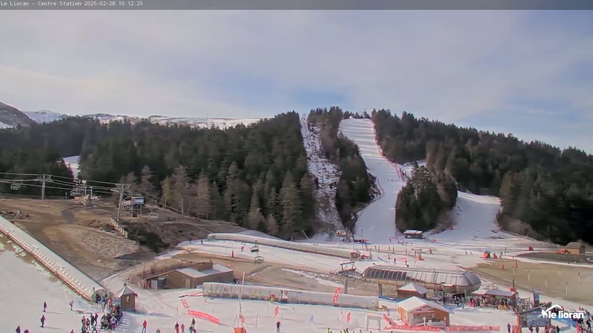 A snowy ski resort with several ski lifts, slopes, and skiers is visible under a partly cloudy sky.