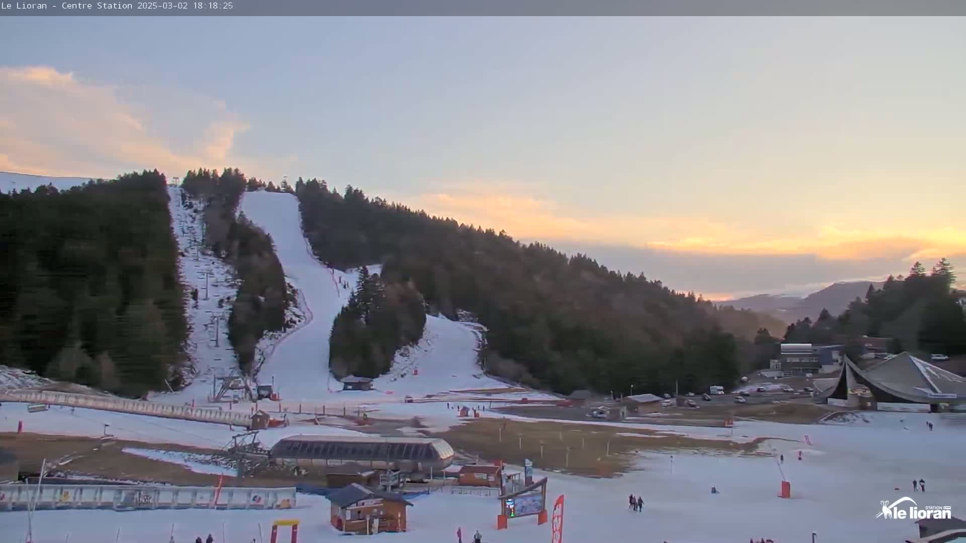 A snow-covered ski slope on a mountainside at sunset under a mostly clear sky.