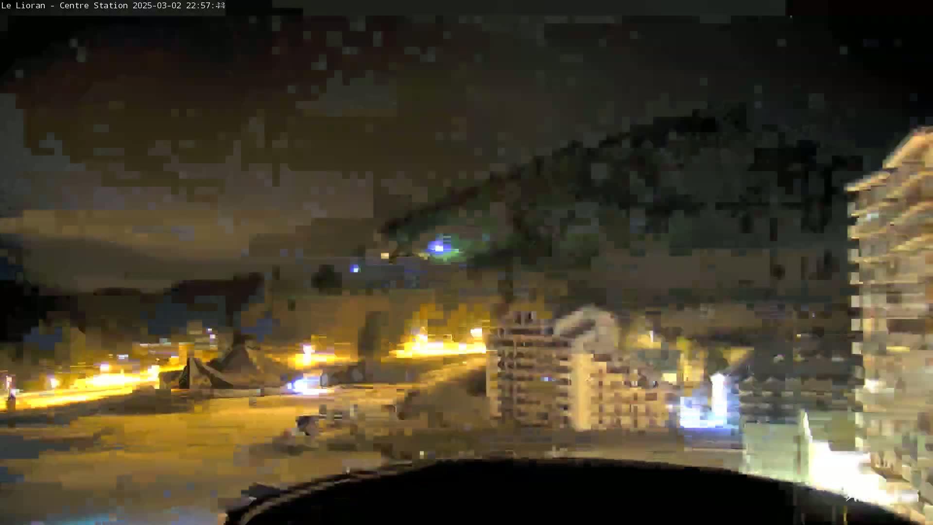 A nighttime view of a snow-covered town with buildings and roads illuminated by lights.