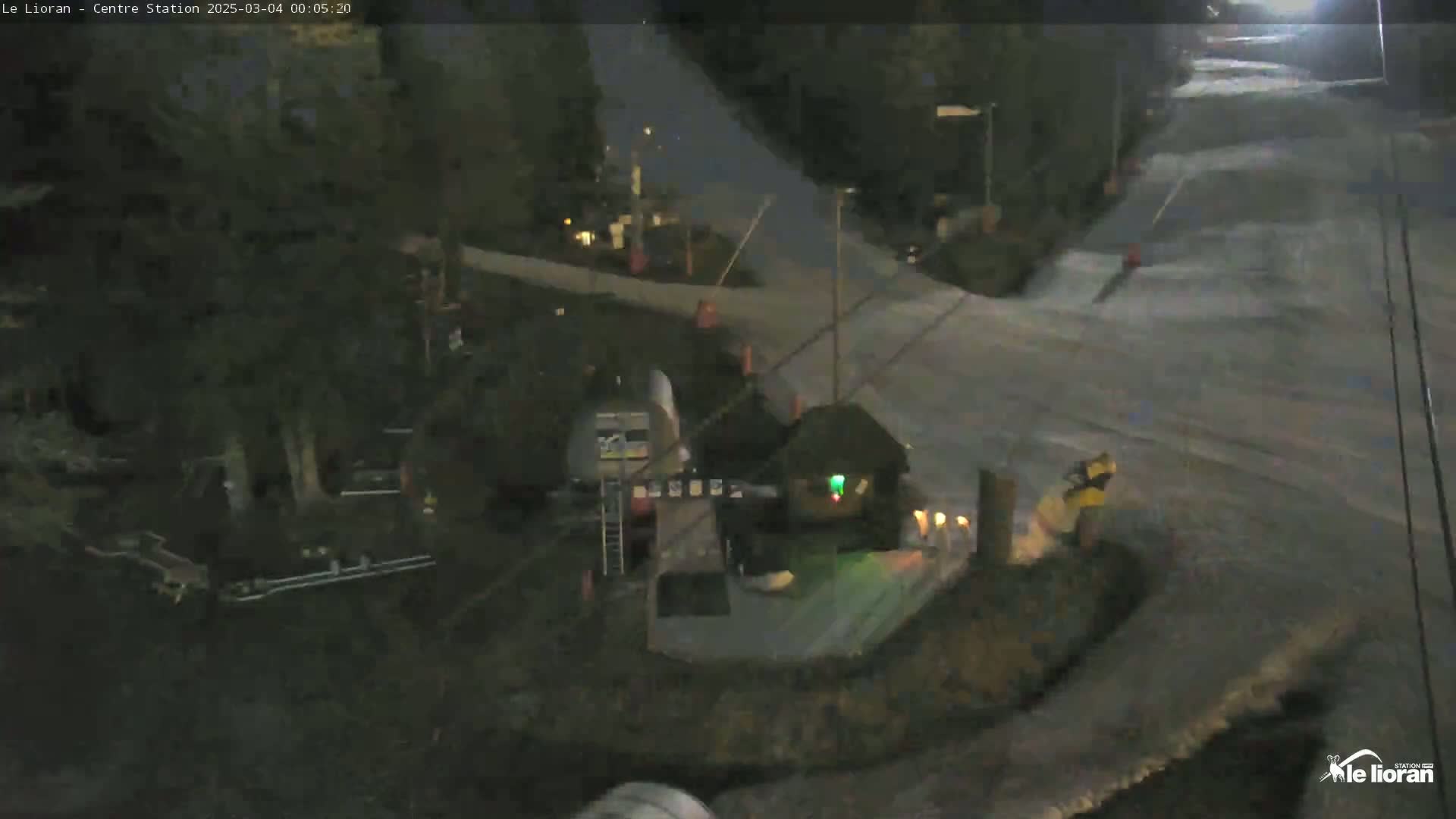 A nighttime, snow-covered ski slope scene shows a small building near a lift and a few people.