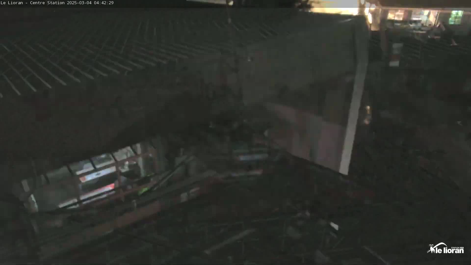 A high-angle, nighttime view shows a dark, partially obscured structure with what appears to be a vehicle or machinery partially visible below.