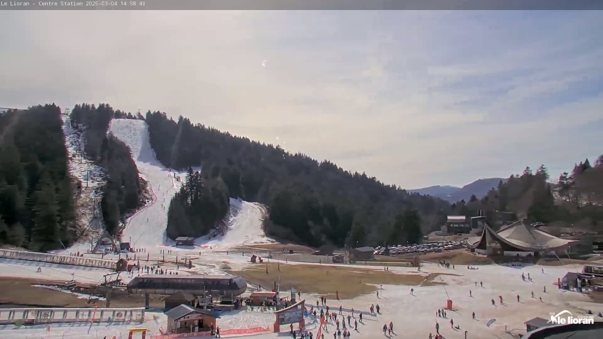 A snow-covered ski resort nestled in a mountainous area under a partly sunny sky.