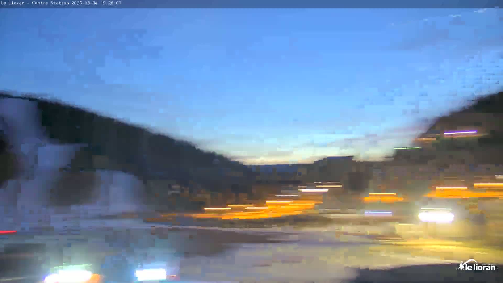 Blurred nighttime traffic moves along a road beneath a clear, twilight sky and dark hills.