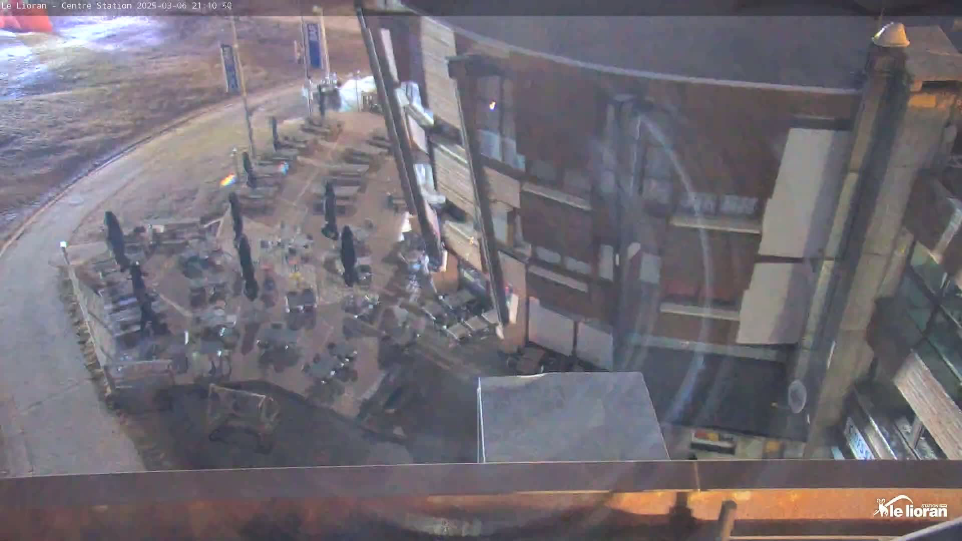 An overhead view shows a mostly empty outdoor patio area next to a multi-story building at night under dark conditions.