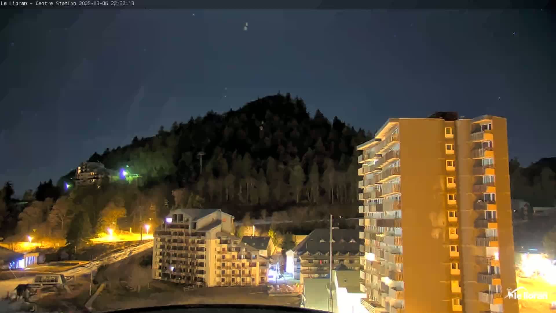 A nighttime view of a mountainside with buildings illuminated, under a clear, dark sky.