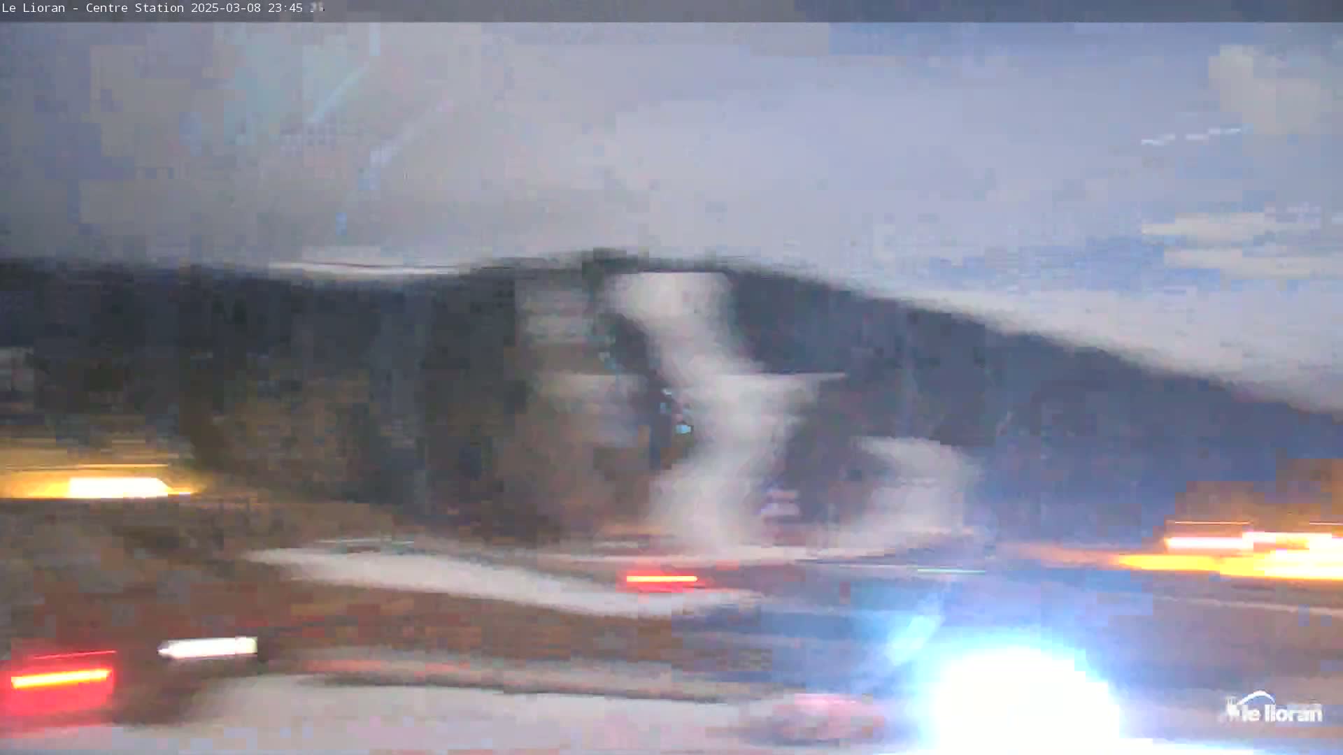 A blurry nighttime view of a highway with several vehicles driving past under a slightly overcast sky.