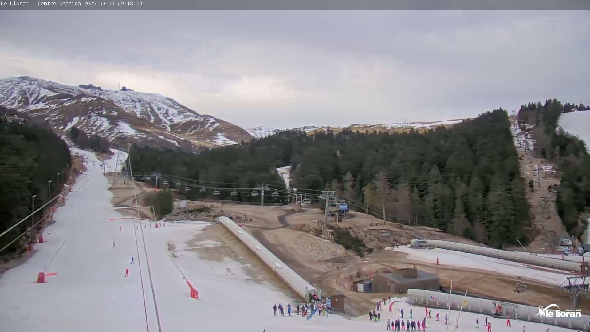 A ski slope with several skiers and chairlifts, situated in a mountainous area under an overcast sky.