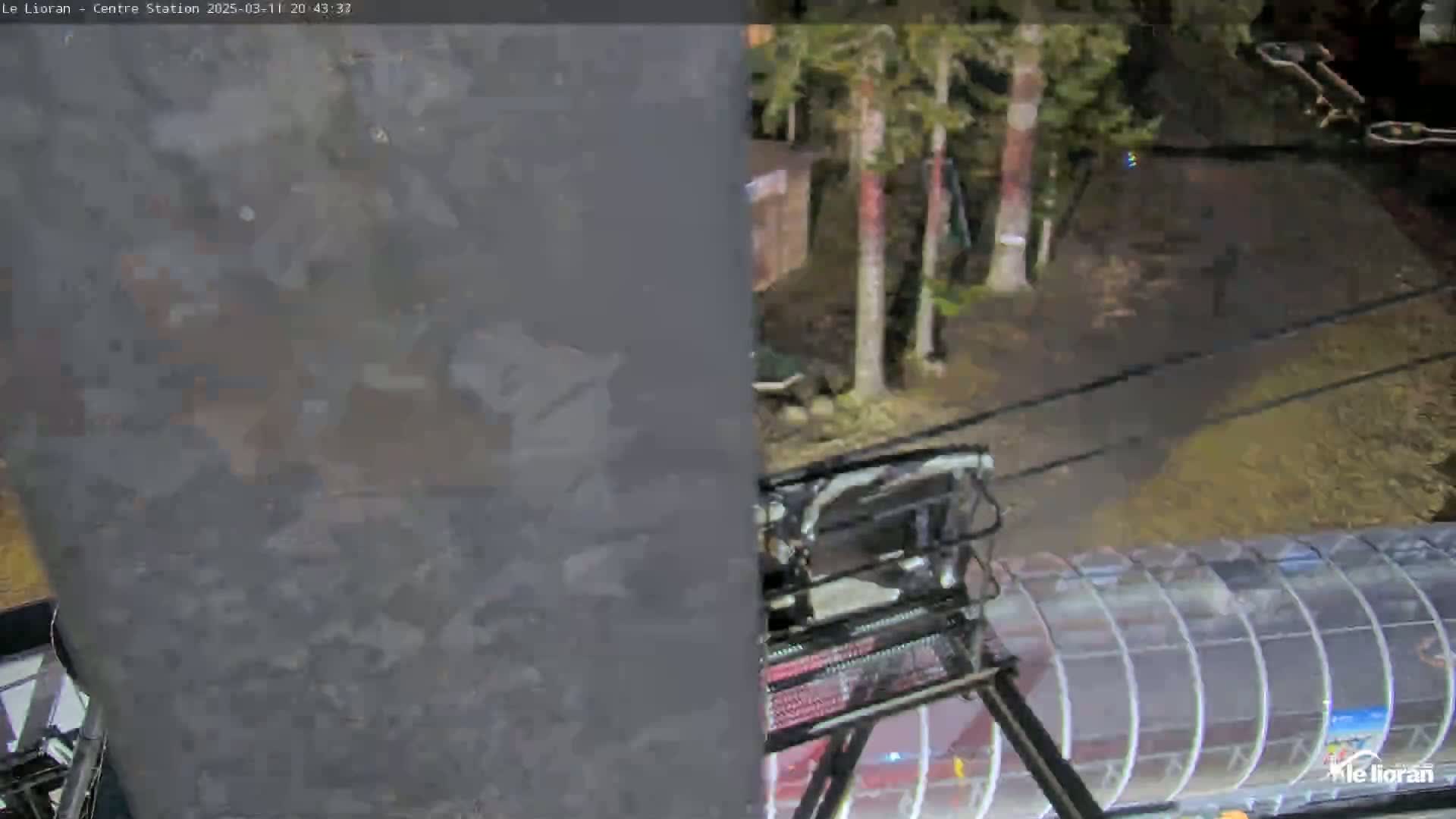 A nighttime view shows a chairlift ascending towards a transparent enclosed structure, passing by several trees in a dark, possibly wooded area.