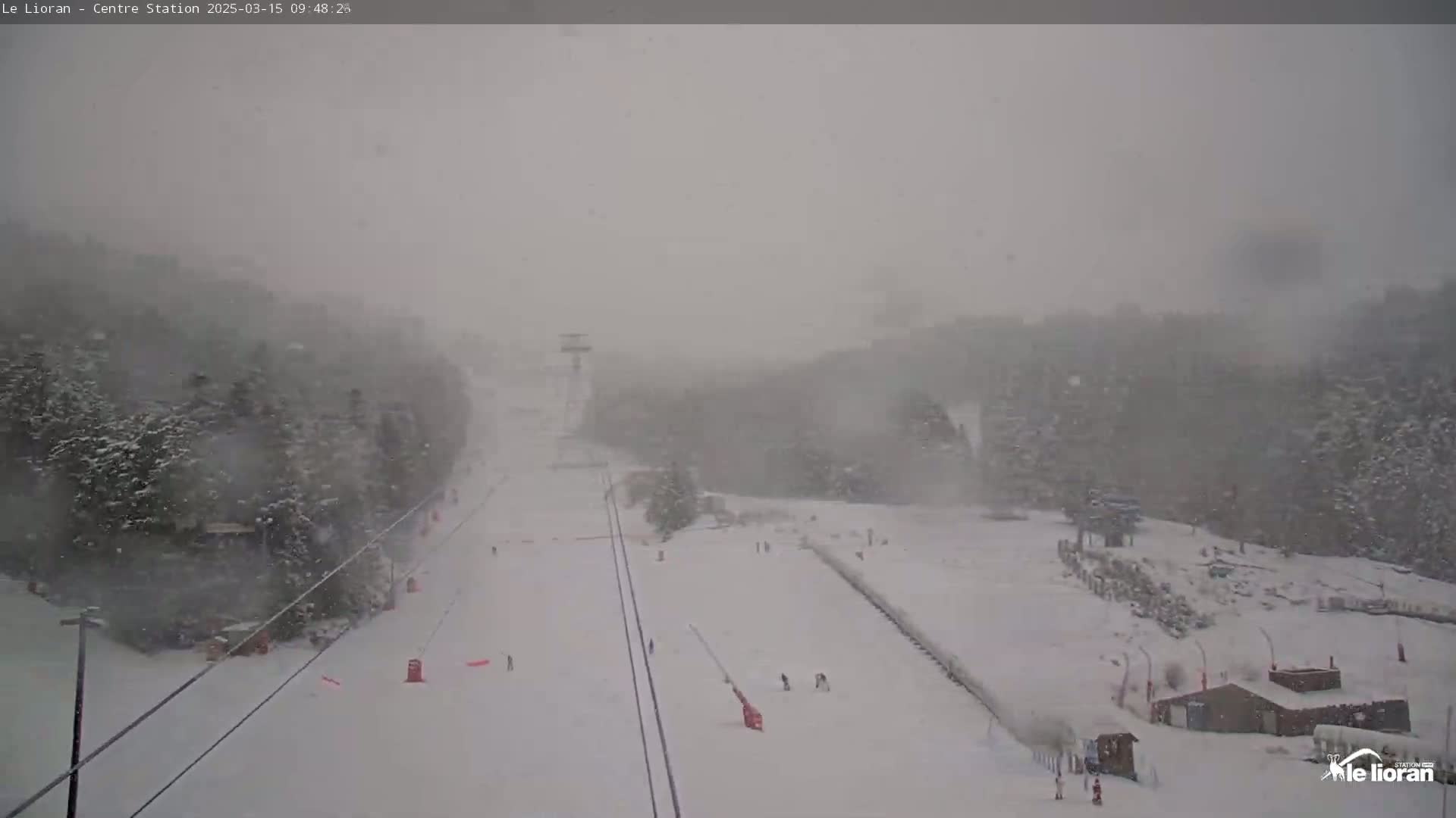 A snow-covered ski slope is visible in heavy snowfall, with a few skiers and a ski lift in the distance.