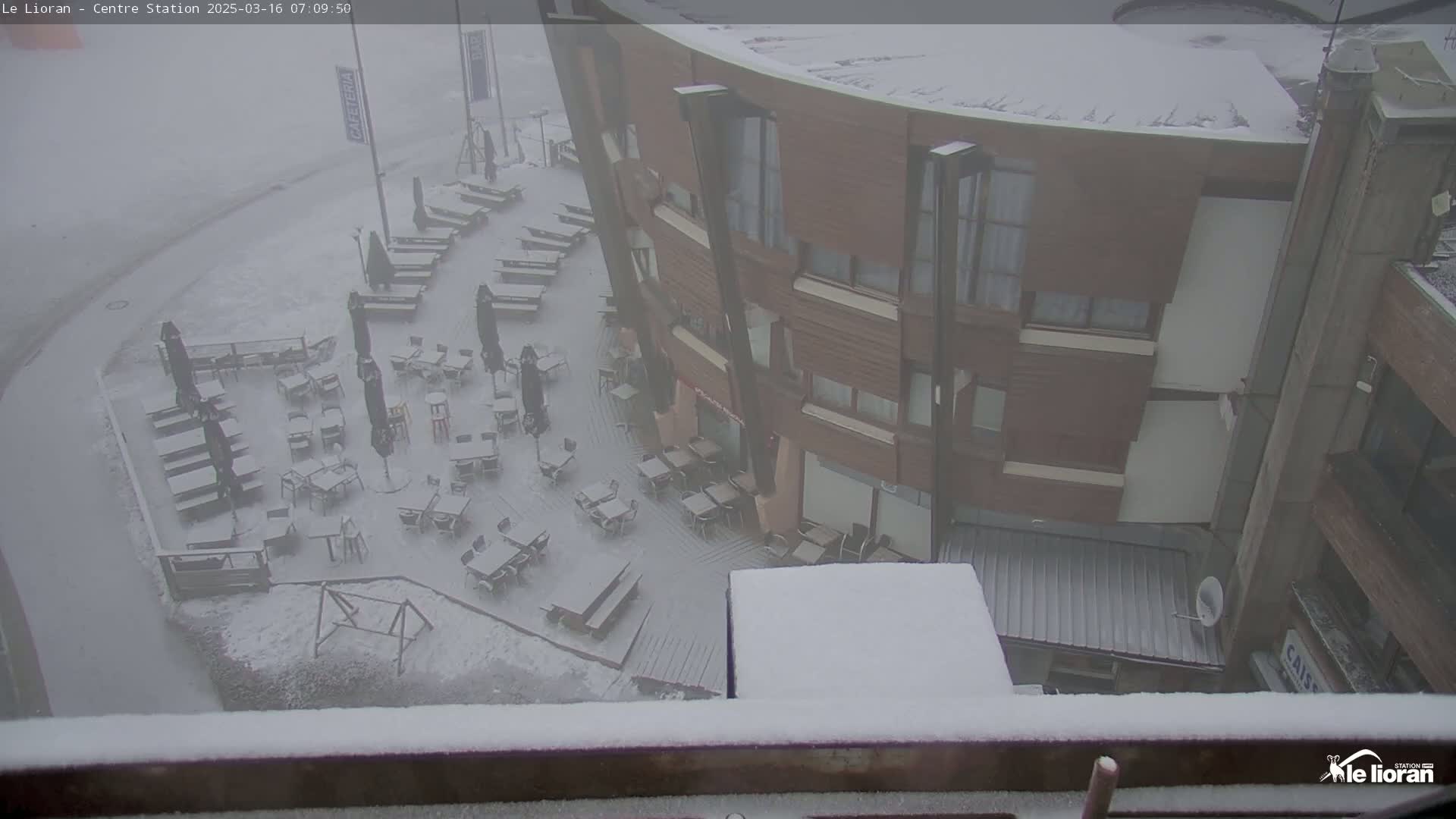 A snow-covered outdoor cafe area sits adjacent to a multi-story building in foggy conditions.