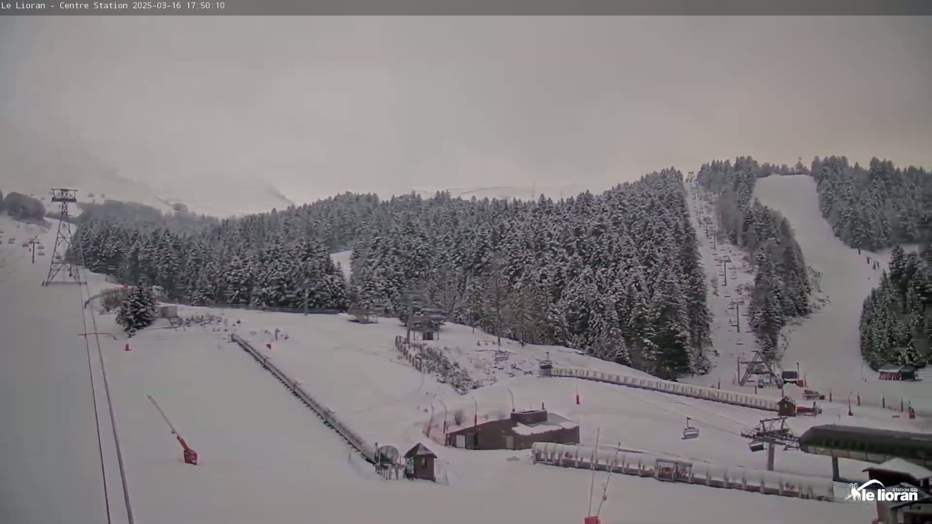 A snow-covered ski resort with chairlifts and runs under an overcast sky.