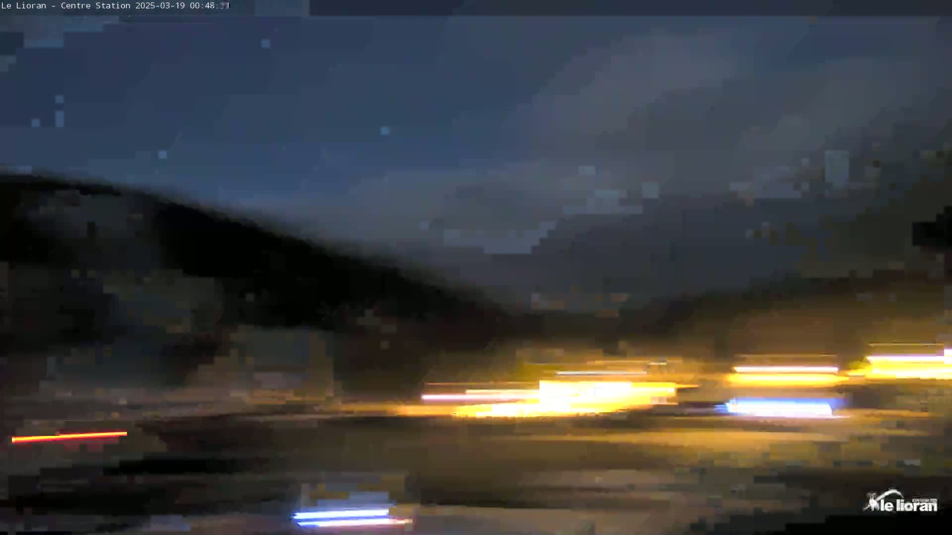 Light streaks from nighttime traffic are visible in front of a dark hill under a mostly clear, dark blue night sky.