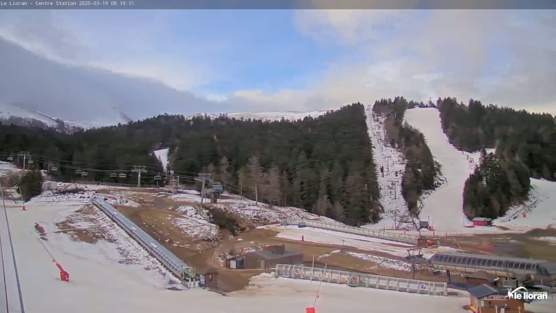 A partly cloudy sky overlooks a snow-covered ski resort with several ski lifts and runs.