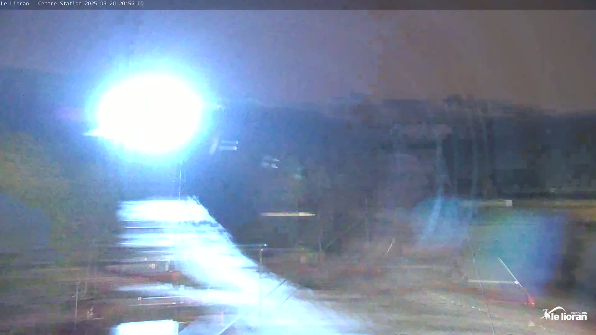 A bright light illuminates a nighttime scene of what appears to be a train station platform with some blurring motion.
