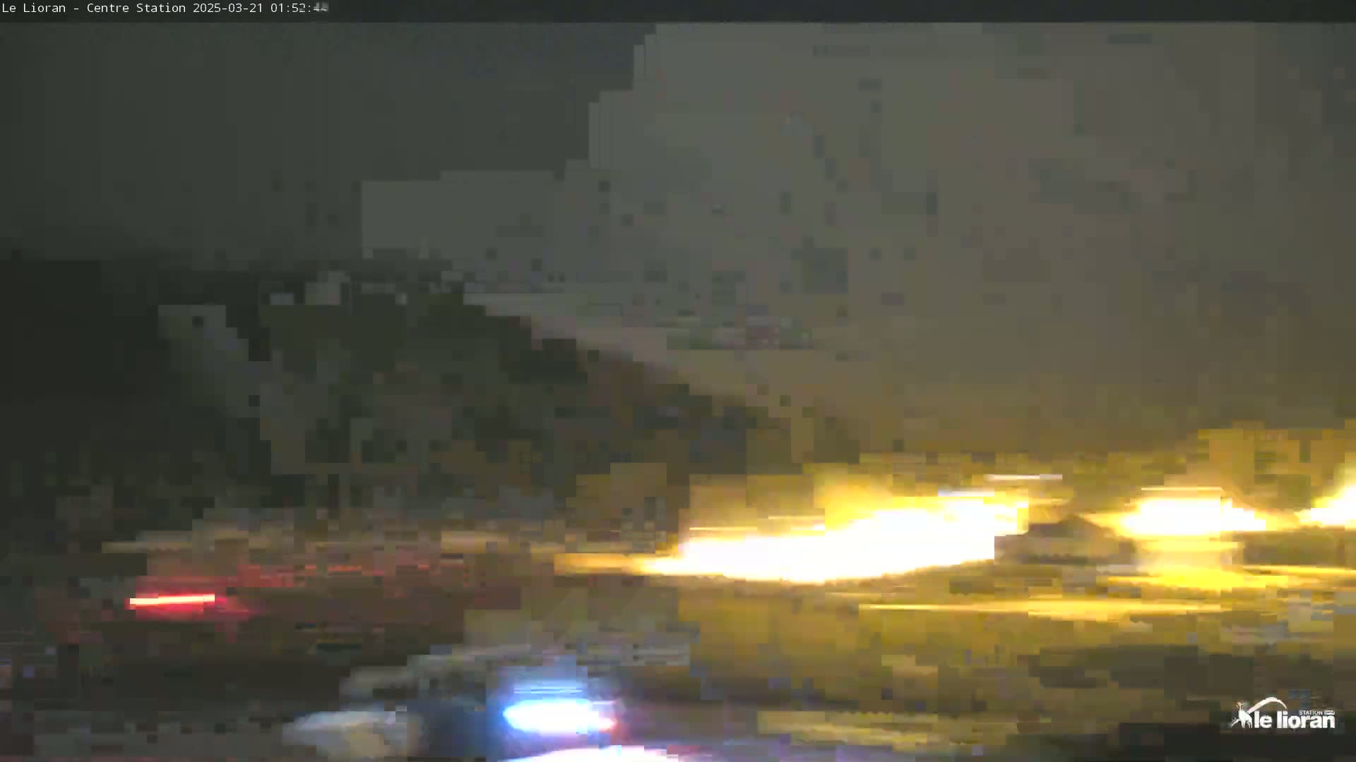 At night, under a dark and hazy sky, headlights from vehicles moving along a road illuminate the scene.