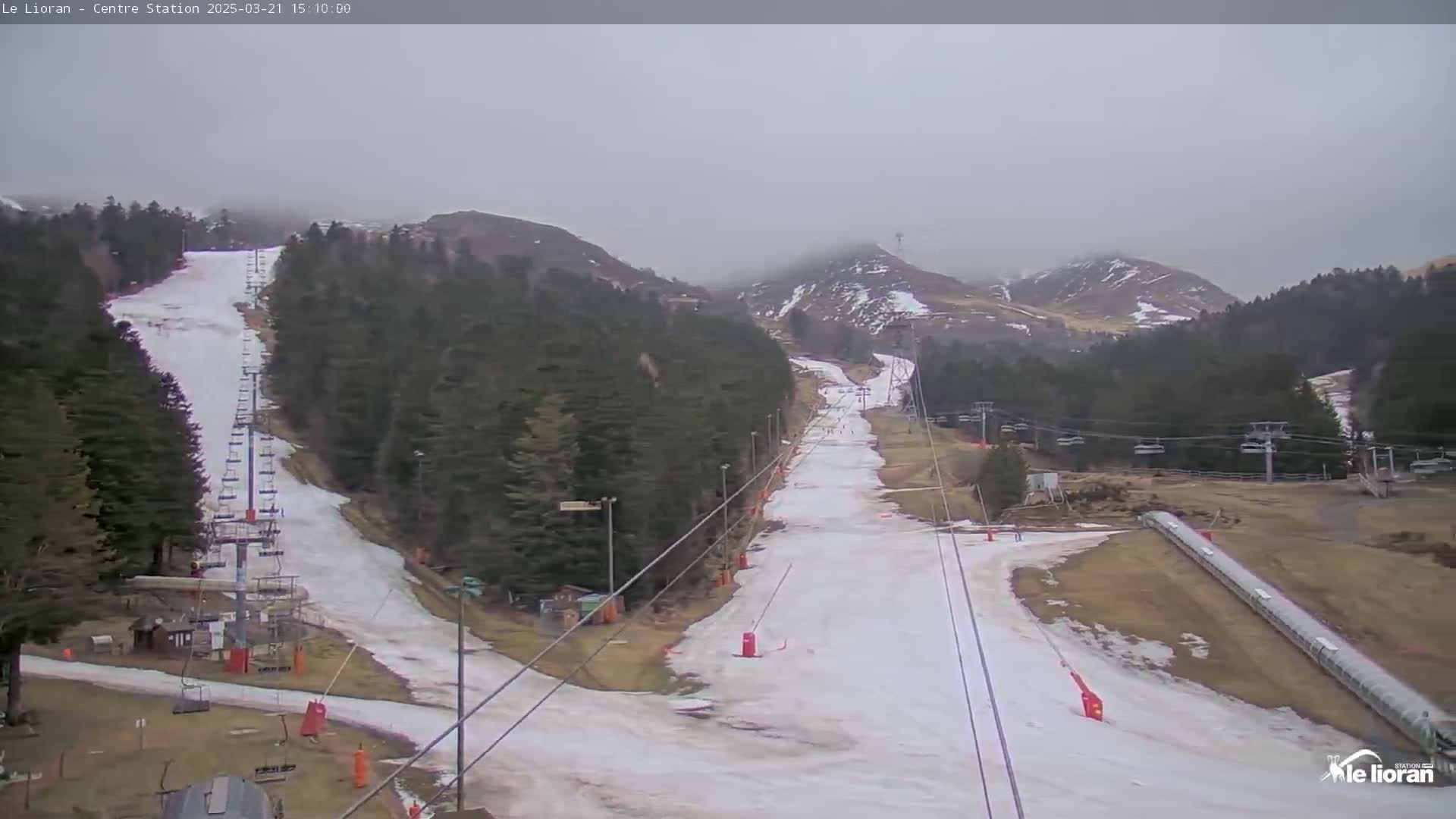 A mostly cloudy day reveals a ski slope with snow, ski lifts, and surrounding evergreen-covered hills.