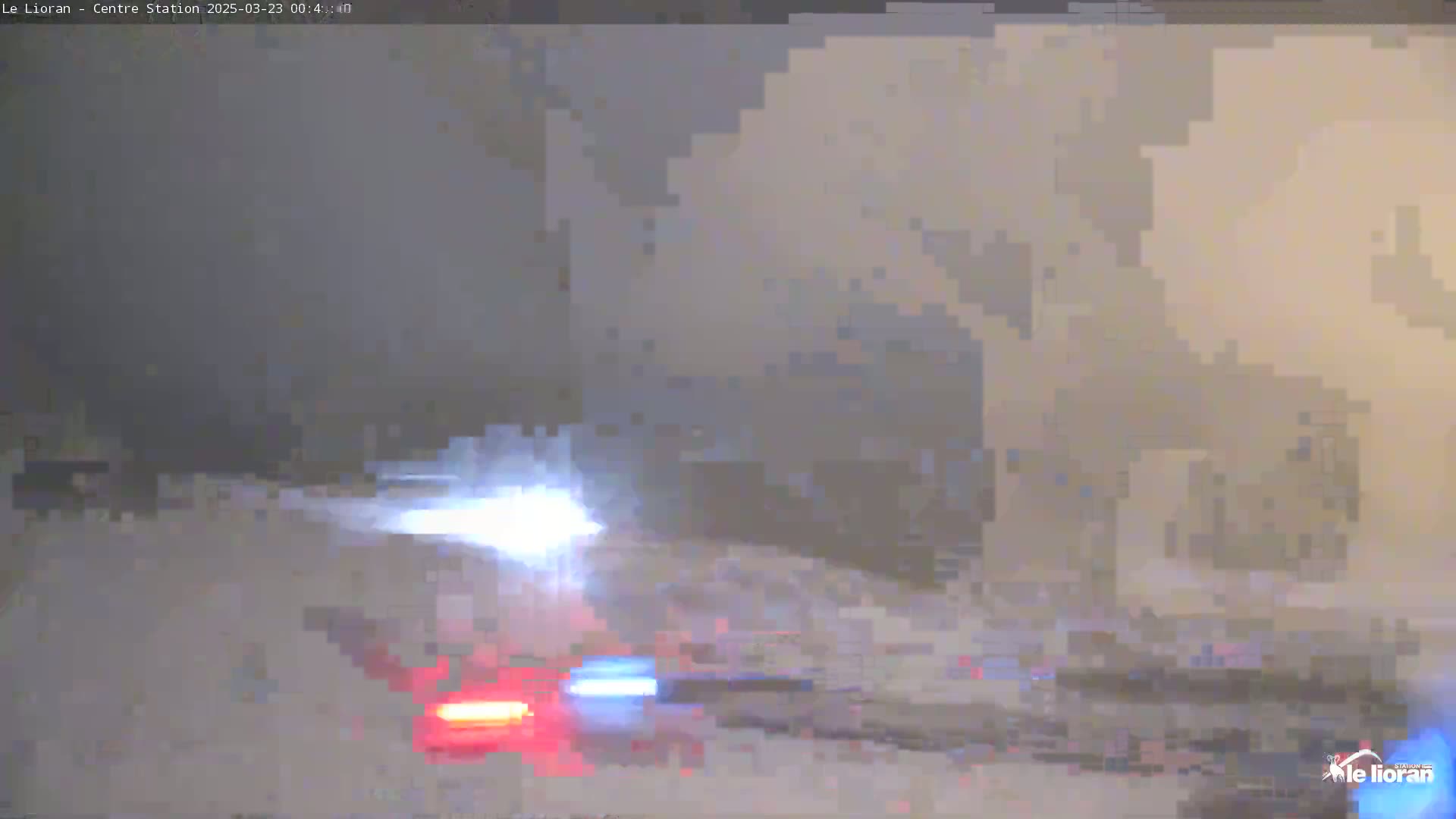 A snowstorm obscures the view of a road where emergency vehicle lights are visible.