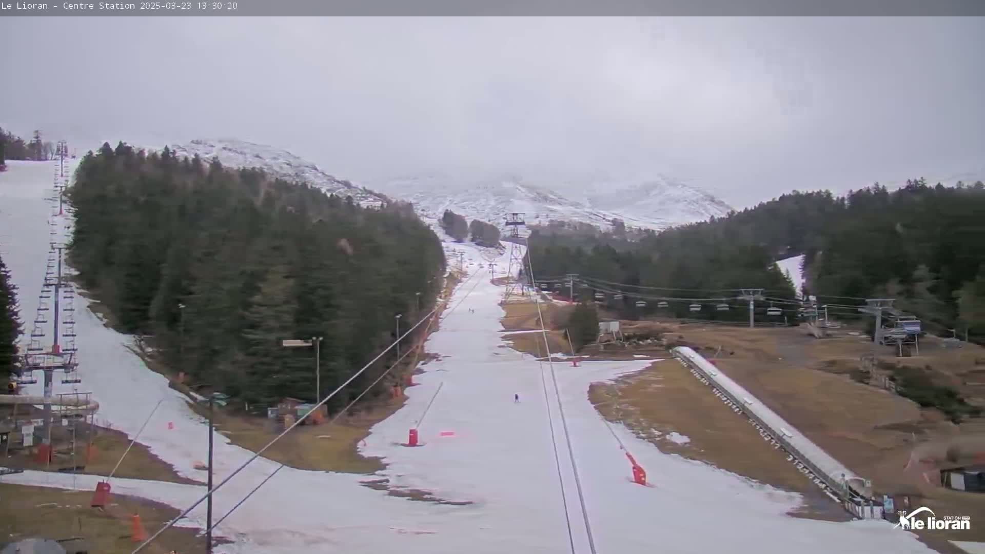 A ski slope with snow-covered runs and chairlifts is visible beneath an overcast sky, surrounded by snow-dusted evergreens and mountains.
