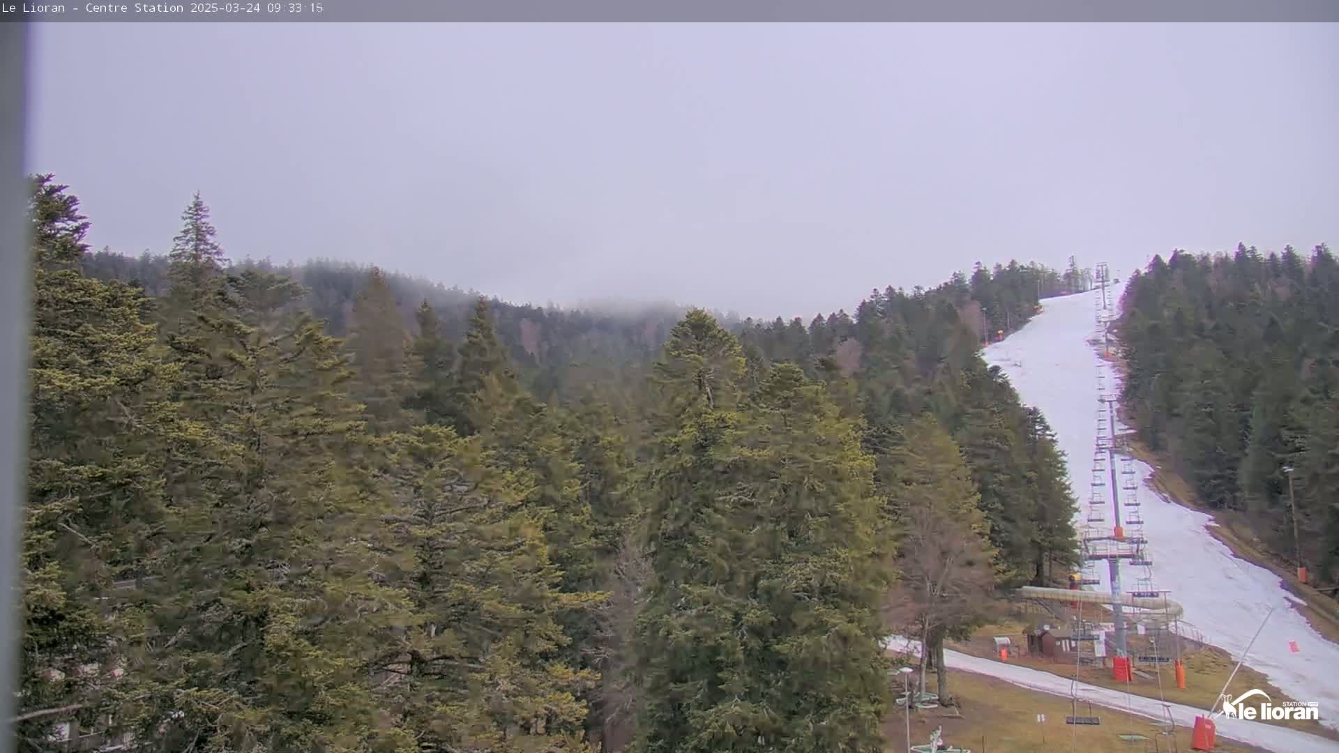 A ski lift ascends a snow-covered slope through a foggy forest of evergreen trees.