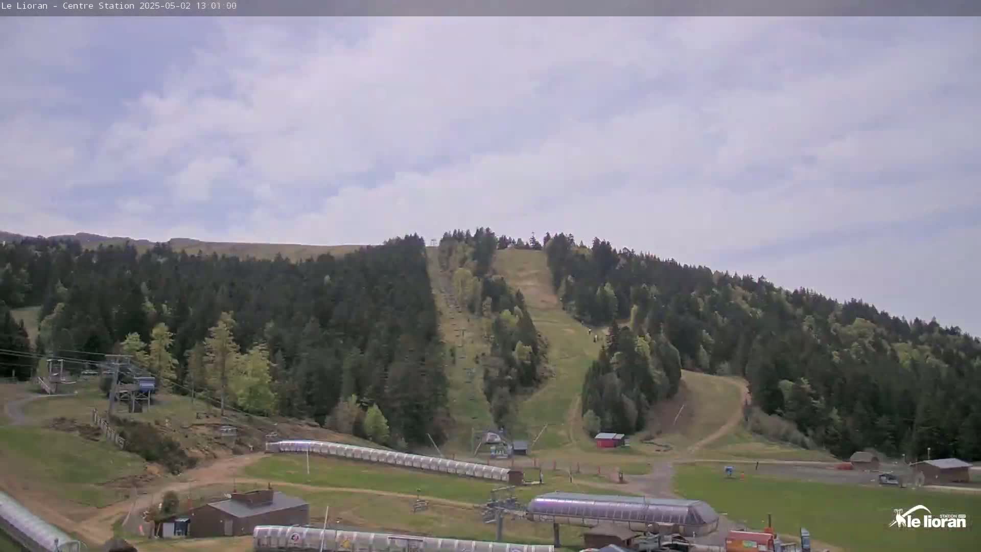 A mostly cloudy day reveals a ski slope nestled in a forest of evergreen trees, with several ski lifts and buildings at the base.
