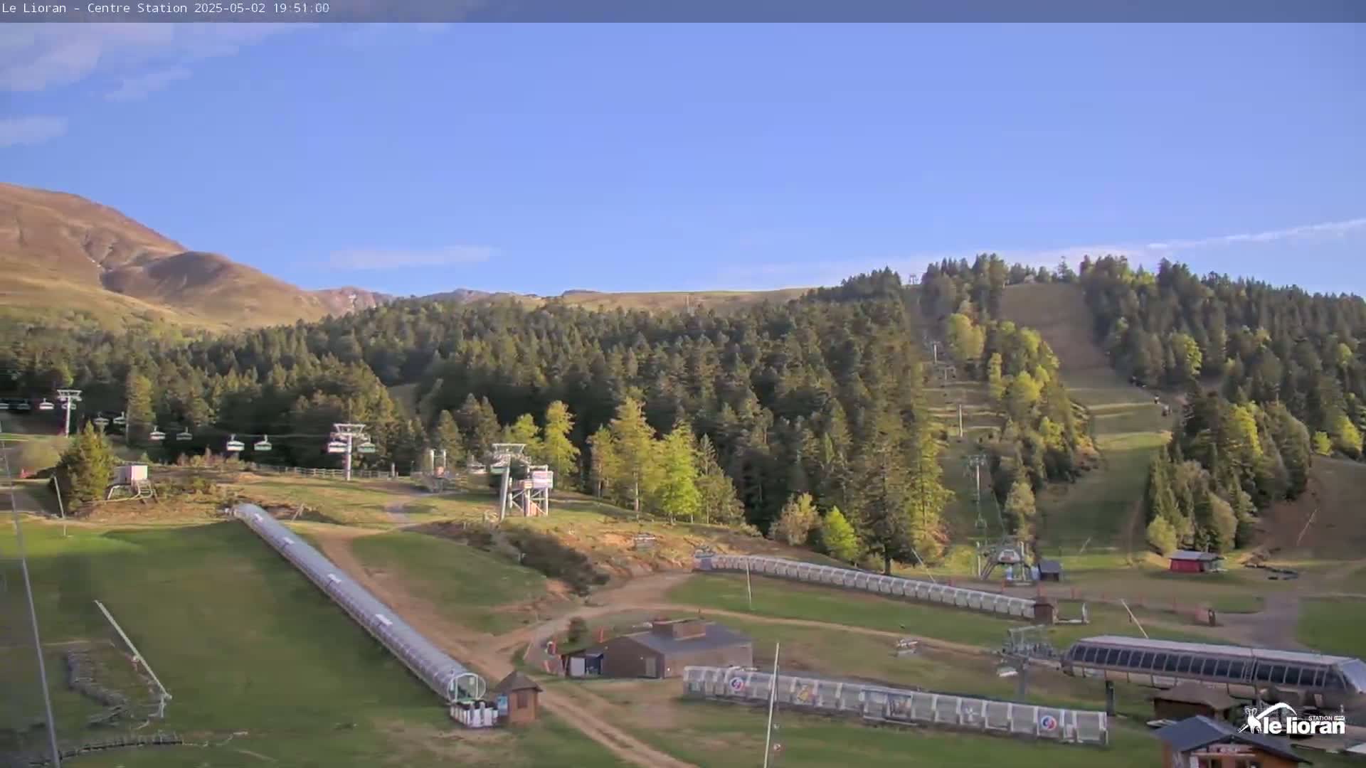 A ski resort in a mountainous area, under a clear blue sky, shows chairlifts, ski runs, and a covered conveyor belt.