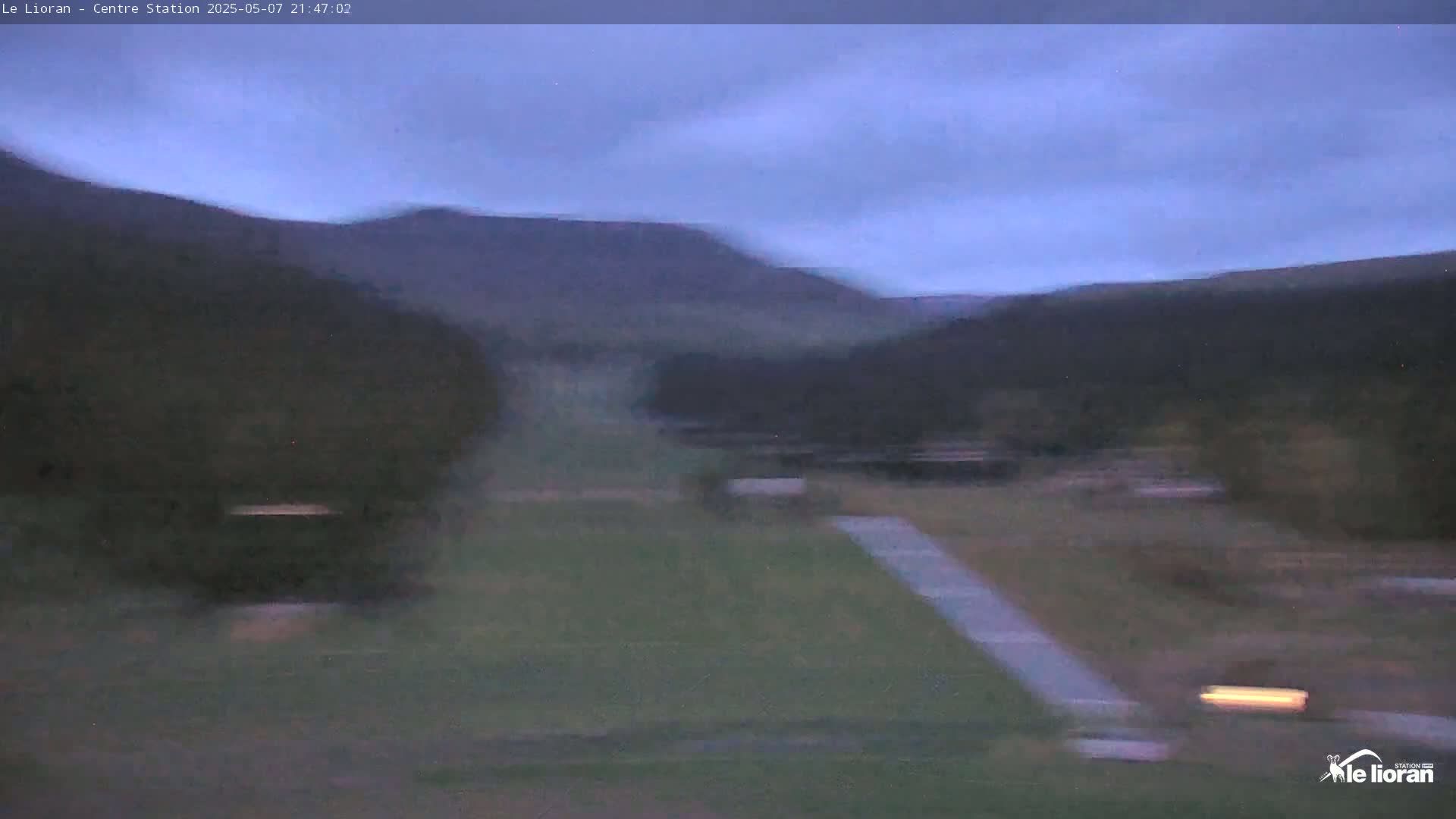 A wide, blurry view of a grassy field under a twilight sky, with dark hills and trees in the background.