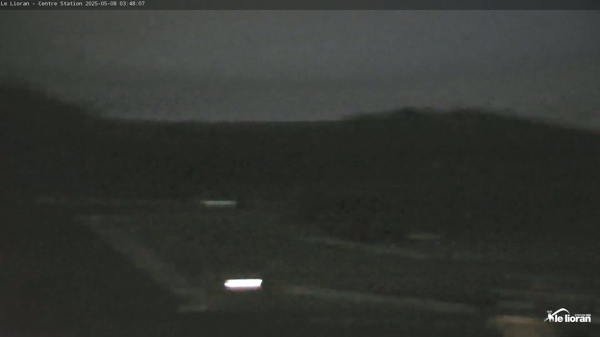 A dark, nighttime scene shows a mostly empty road leading towards a hill under a cloudy sky.