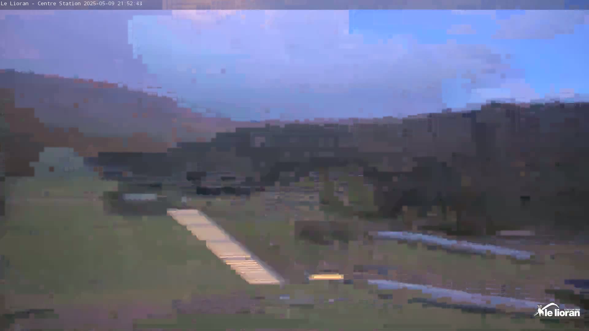 A mostly clear twilight sky illuminates a grassy area with a light-colored walkway leading towards a dark, indistinct structure in the distance.