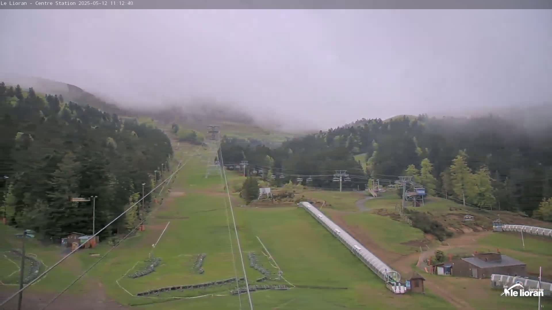 A foggy, overcast view of a ski resort with chairlifts, grassy slopes, and a covered moving walkway.