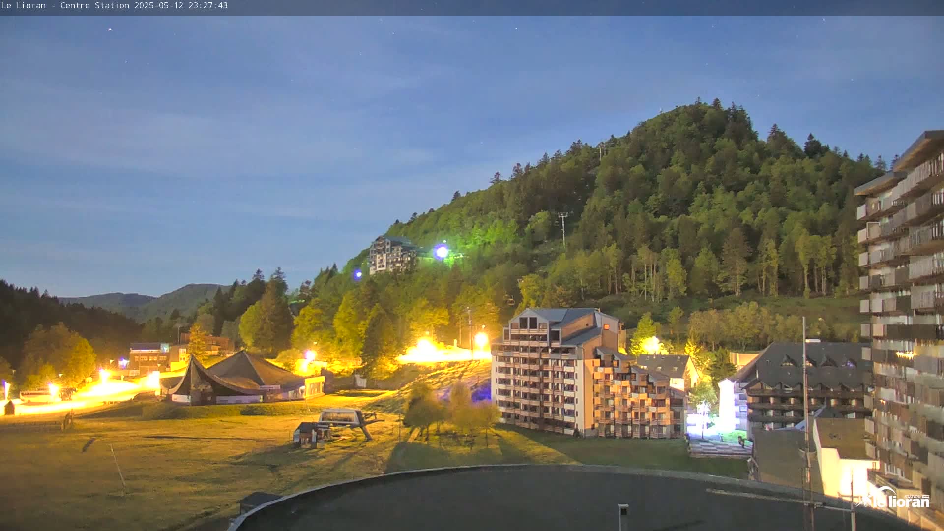 A nighttime view of a mountainside resort town, illuminated by artificial lights under a twilight sky.