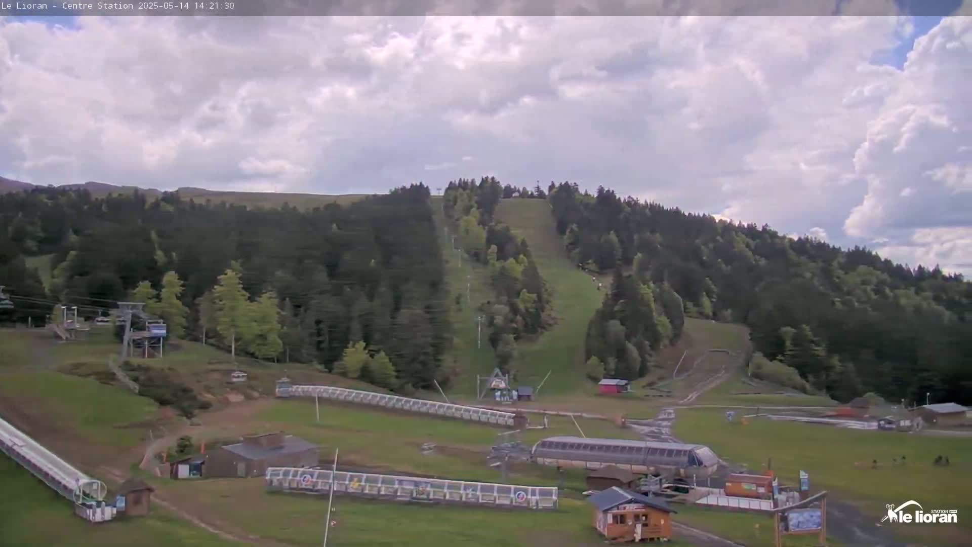 A mostly cloudy sky overlooks a grassy ski resort with chairlifts, ski runs, and other infrastructure.