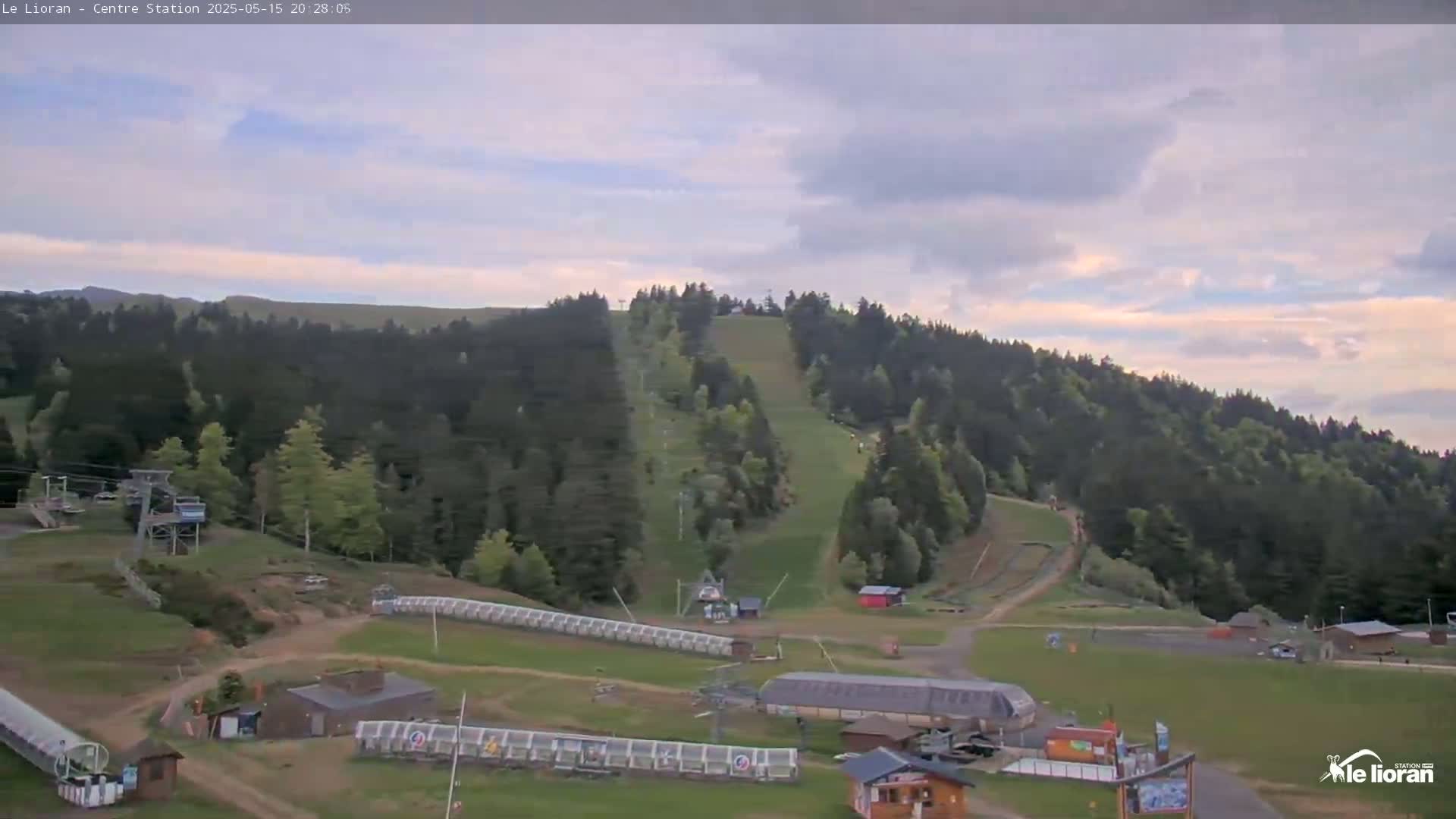 A ski resort in a forest-covered mountain range under a partly cloudy sky.