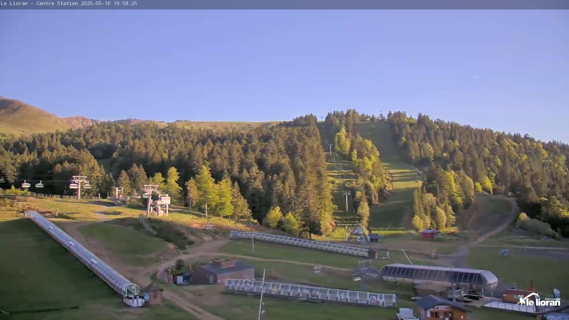 A ski resort in the mountains on a clear, sunny day shows several chairlifts, ski slopes, and support buildings.