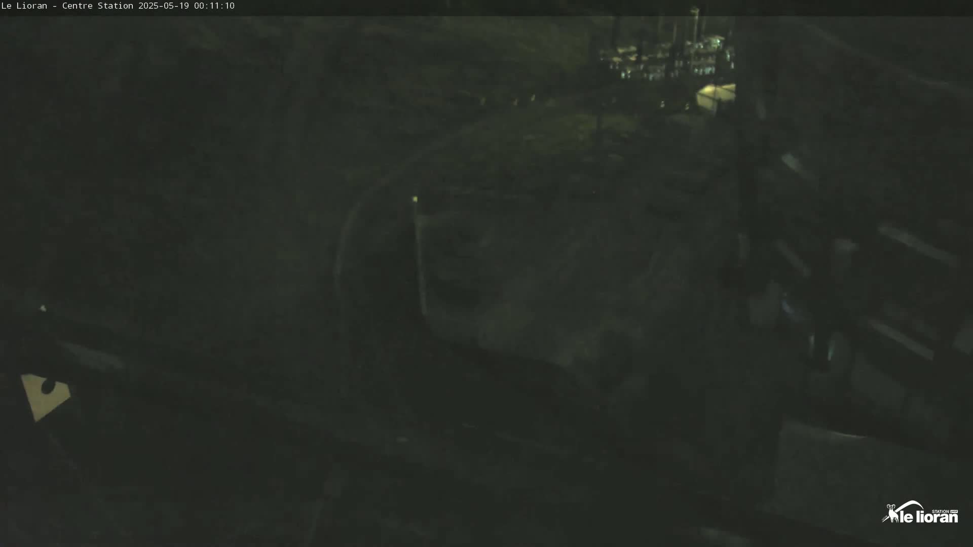 A dark, nighttime view shows a mostly empty paved area with some indistinct structures and faint lighting.