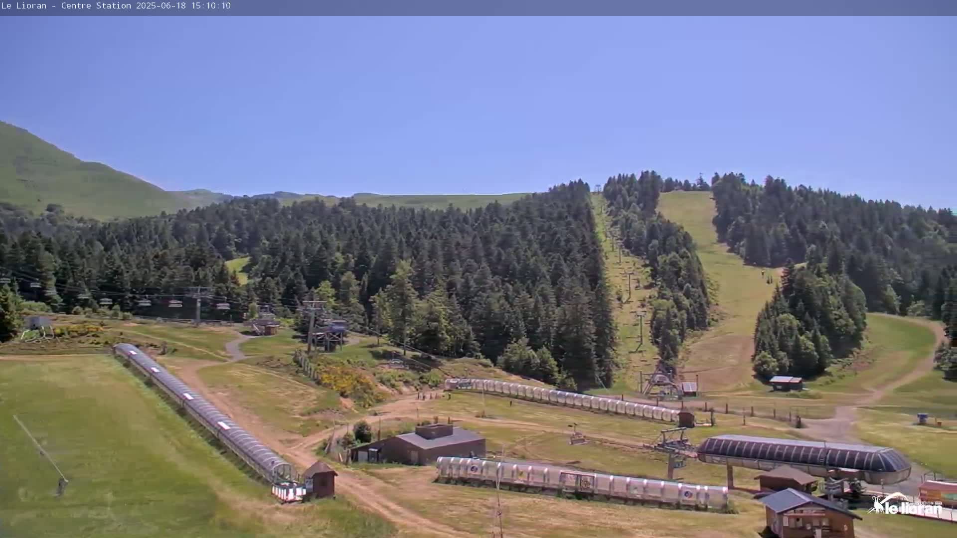 A mountainside ski resort with chairlifts and covered conveyor belts is visible under a clear blue sky.