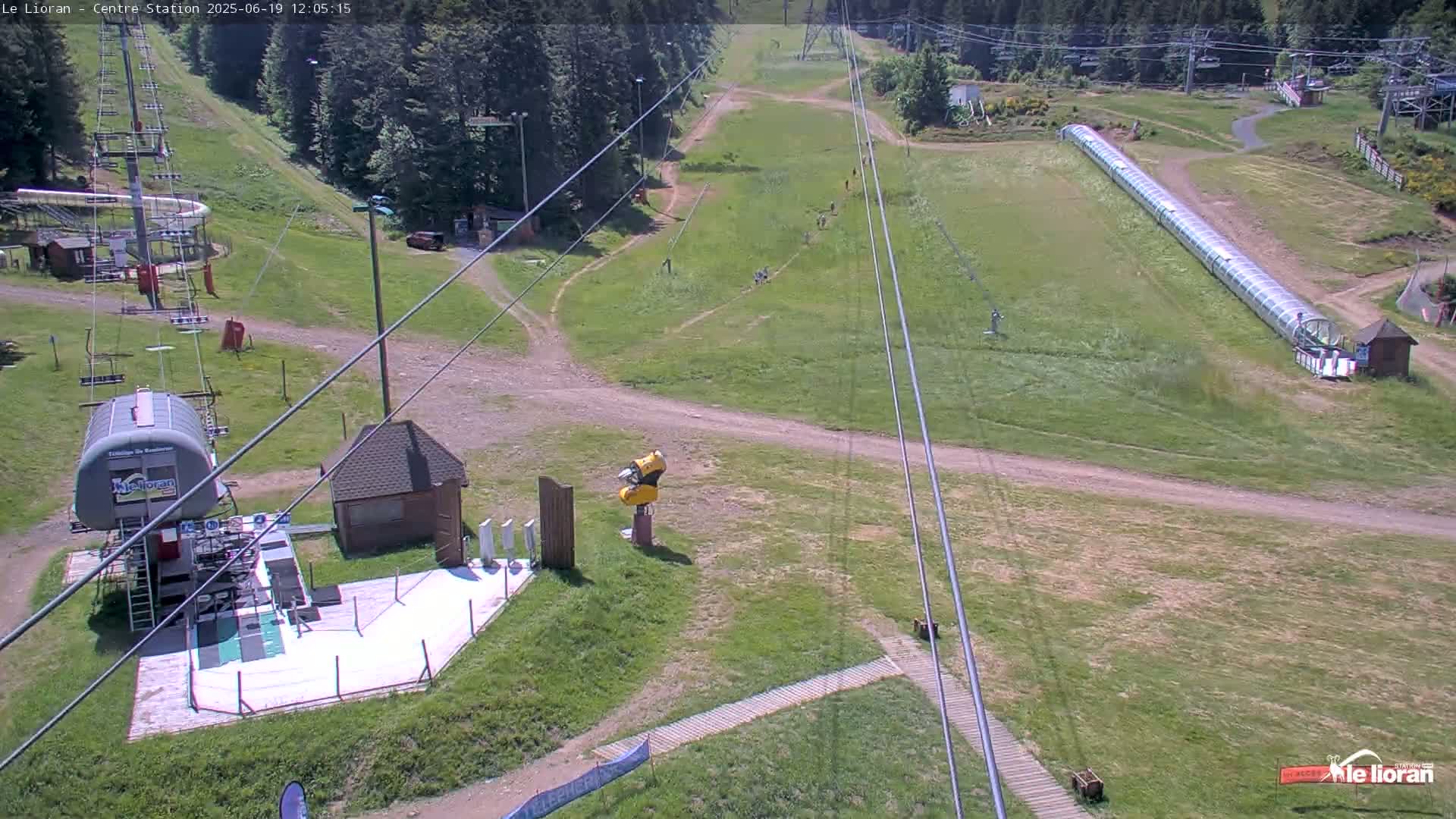 An overhead view of a ski resort in summer shows grassy hills, a chairlift, and a long, covered snow-tubing run.