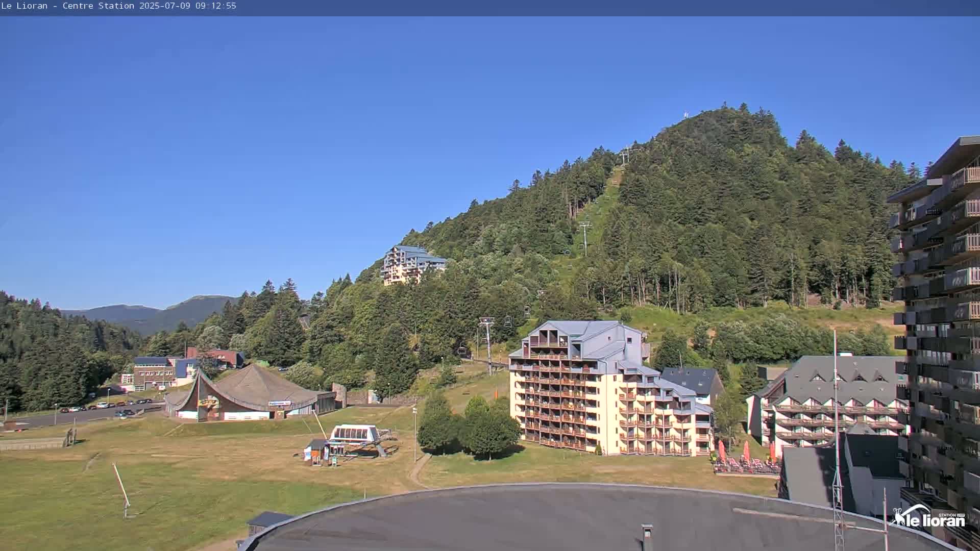 A sunny view of a mountainside resort with several buildings, chairlifts, and grassy areas.