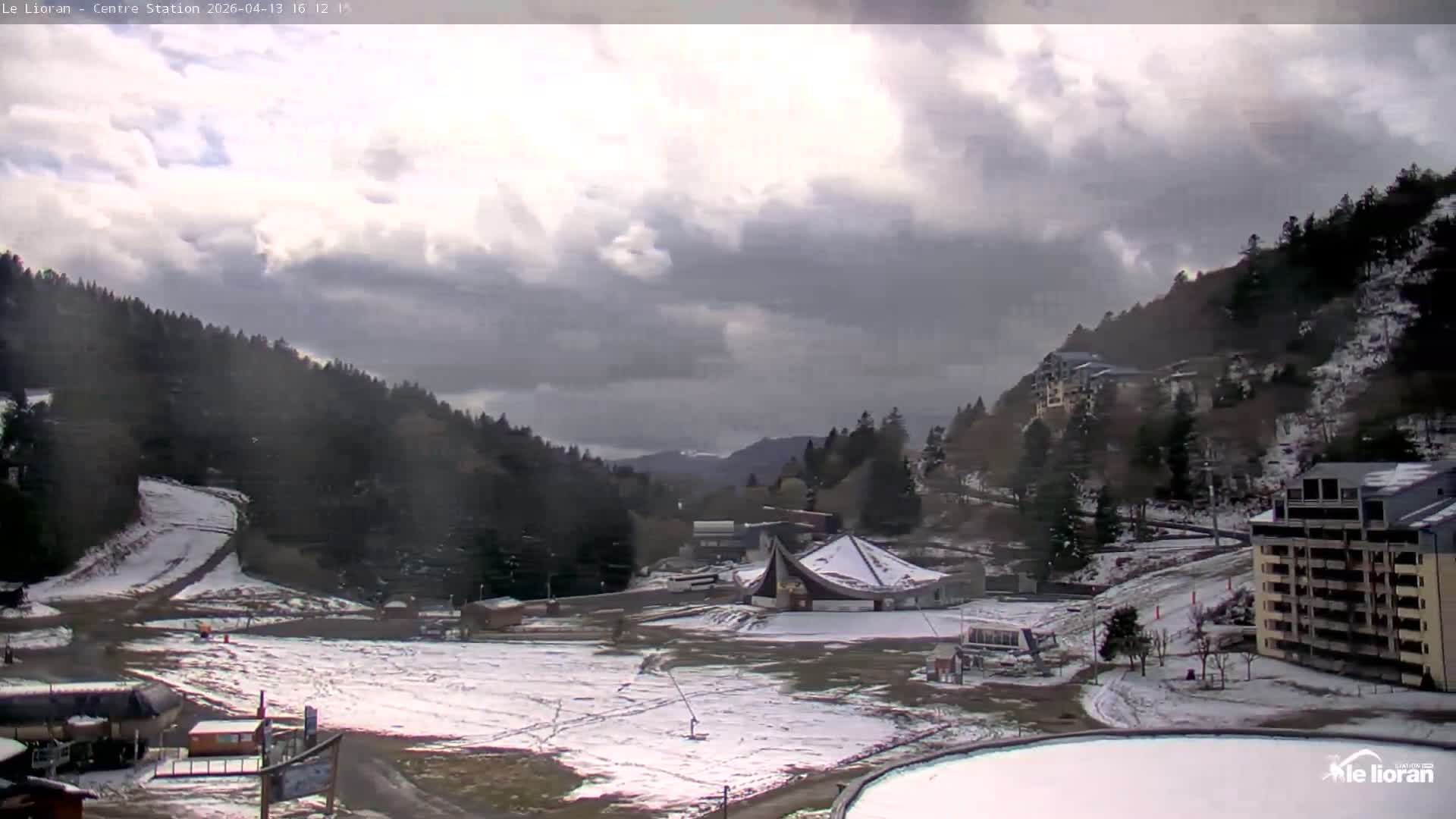 A sunny view of a mountainside resort with several buildings, chairlifts, and grassy areas.