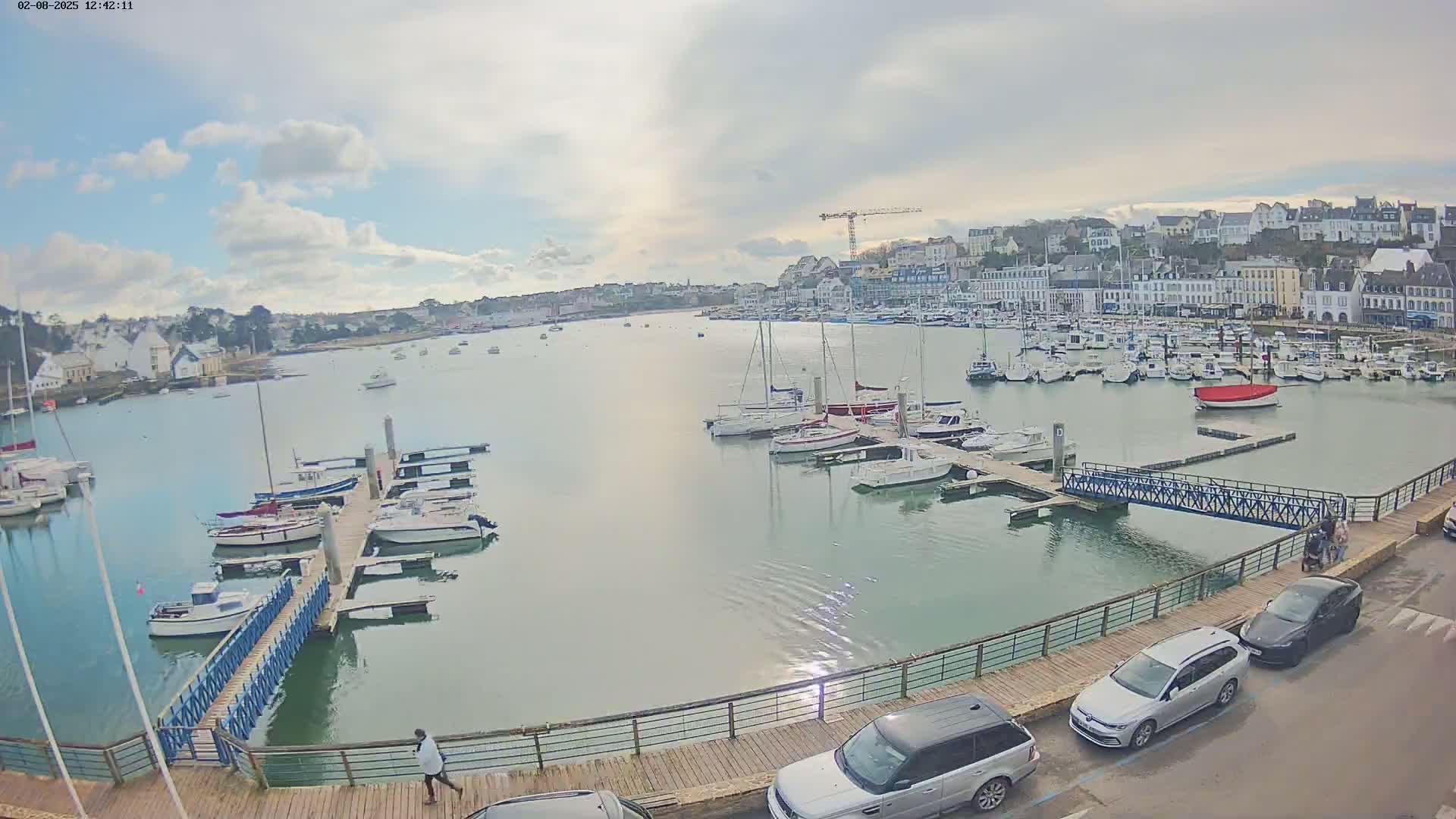 A harbor filled with numerous boats and yachts is situated in front of a town under a partly cloudy sky.