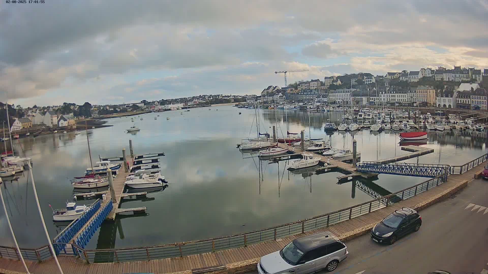 A harbor filled with numerous boats and yachts under a cloudy sky, with a town in the background.