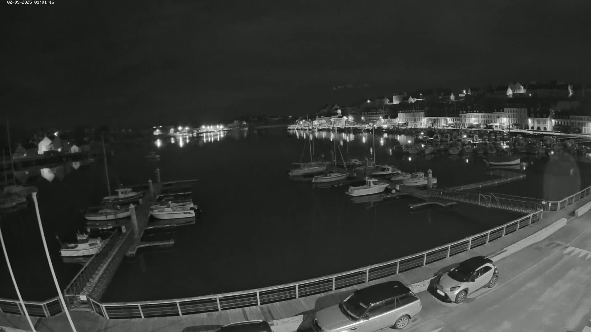 A nighttime view of a harbor filled with boats, alongside a town with lights reflecting on the water.