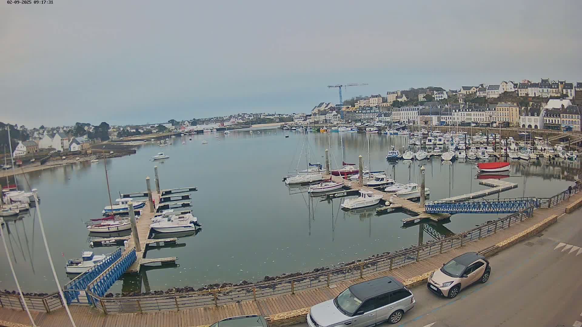 A harbor filled with numerous boats and yachts on a calm, overcast day, with a town visible in the background.