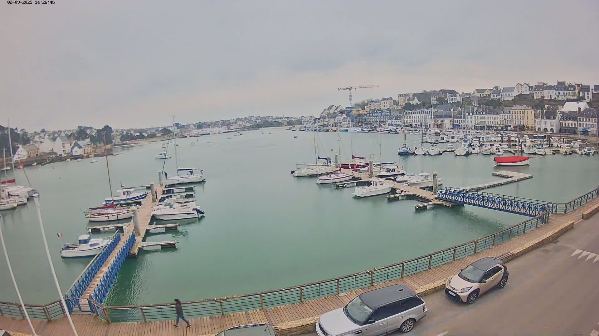 A harbor filled with sailboats and motorboats on a cloudy day, with a town visible in the background.