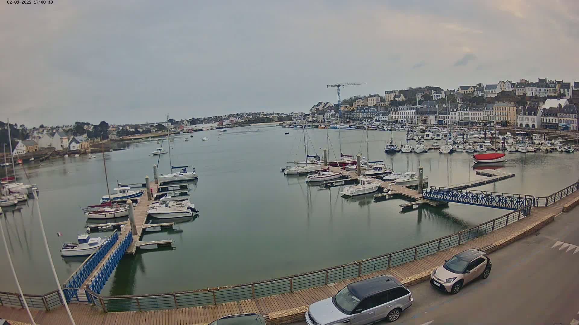 A harbor filled with numerous boats and yachts under an overcast sky, with a town visible in the background.