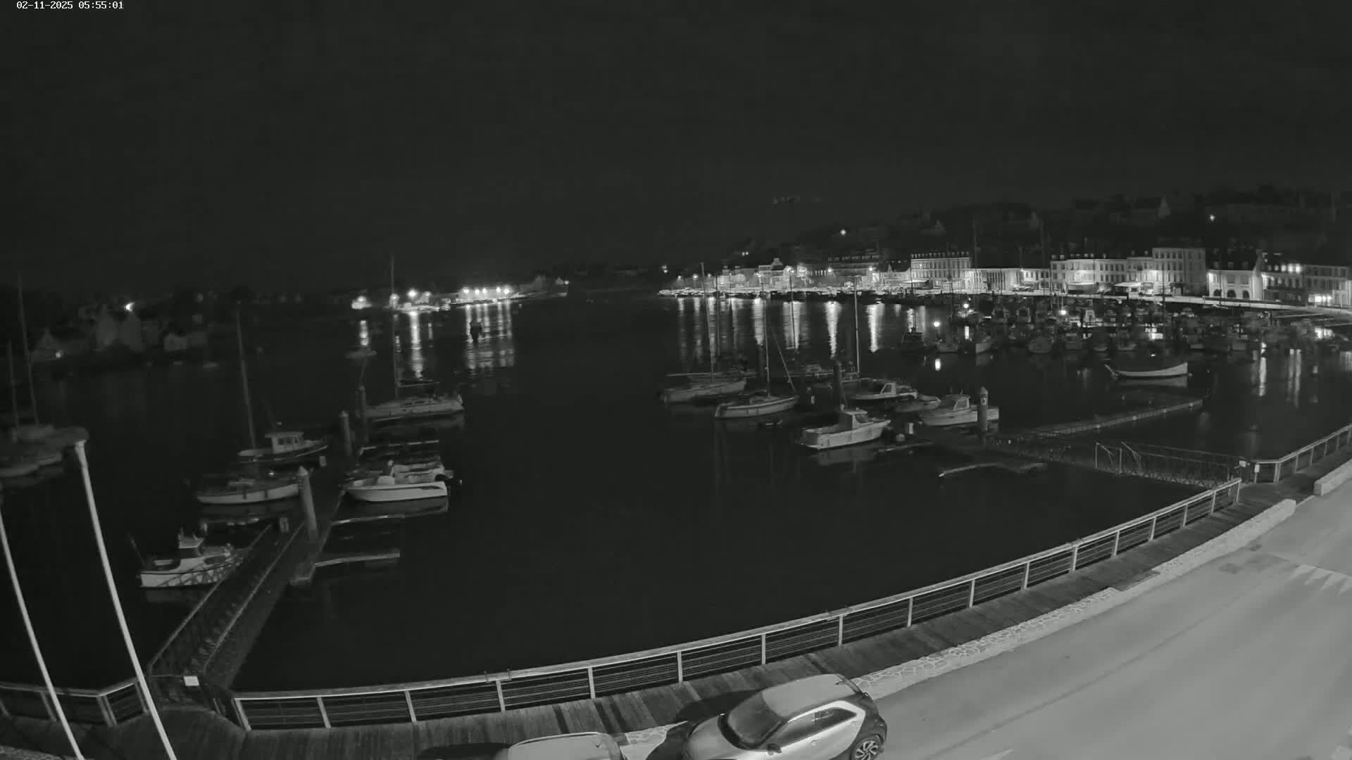 At night, a harbor filled with numerous boats is illuminated by lights from buildings along the shore.